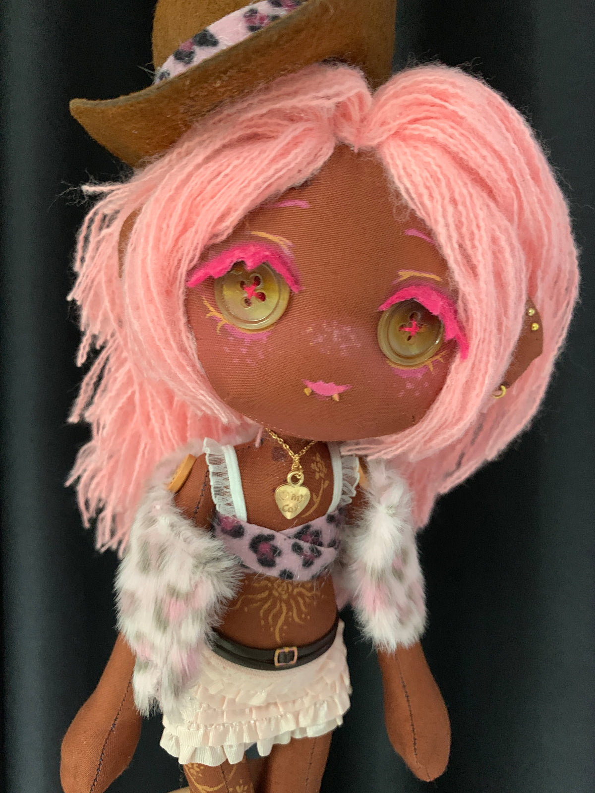 Close-up portrait of Coco Berry handmade rag doll showing button eyes, pink yarn hair, elven ear piercings, and heart necklace.